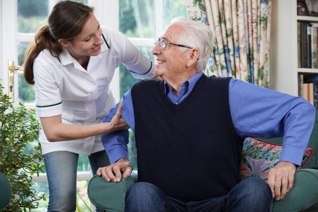 A woman is helping an older man sit on the couch.