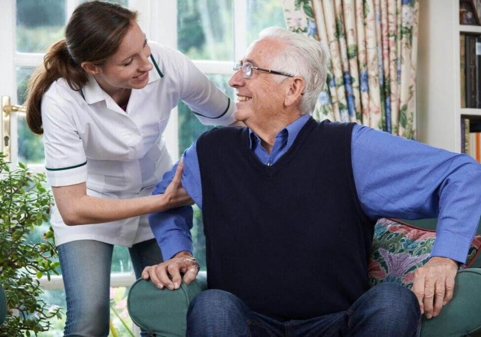 A woman is helping an older man sit on the couch.